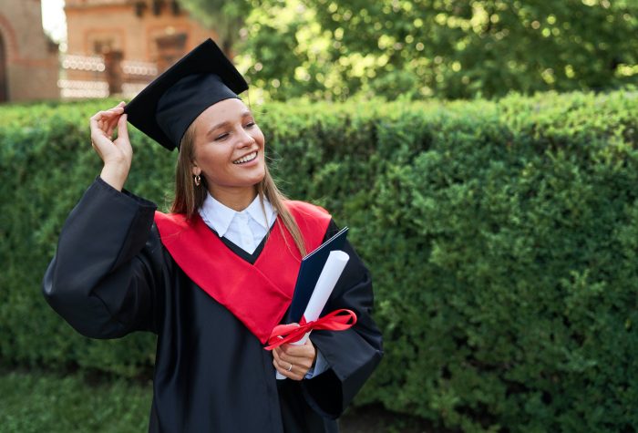 Portrait of young pretty graduate student girl in graduating robe and with diploma, copy space for text.